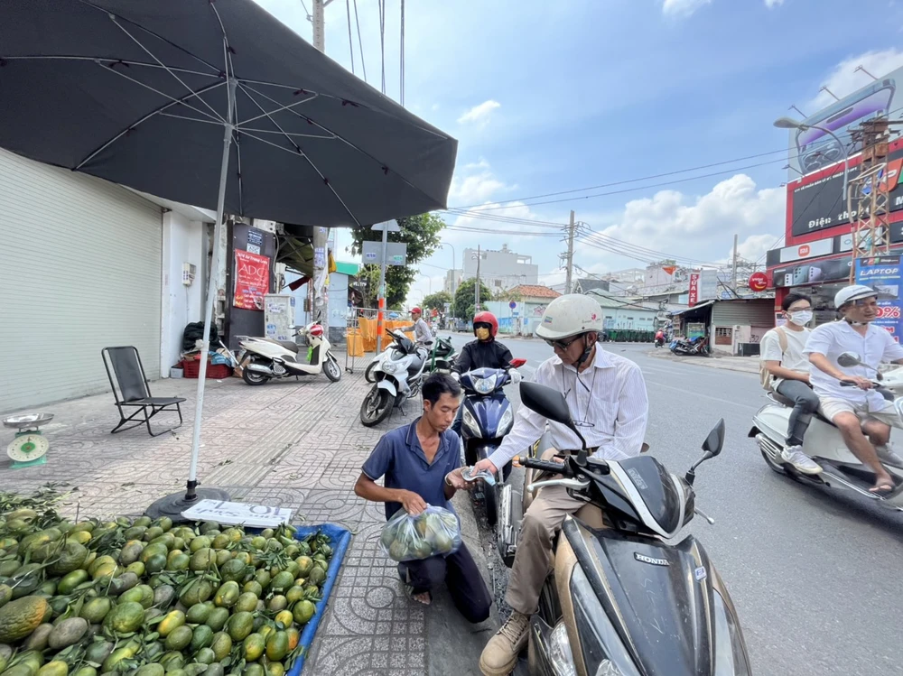 Một người dân nhờ người bán chọn cam, cân kí xong và trả tiền.
