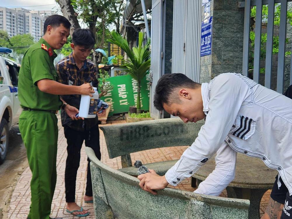 Công an hướng dẫn và giám sát cả ba người lau chùi lại vết sơn quảng cáo đã xịt. Ảnh: TS