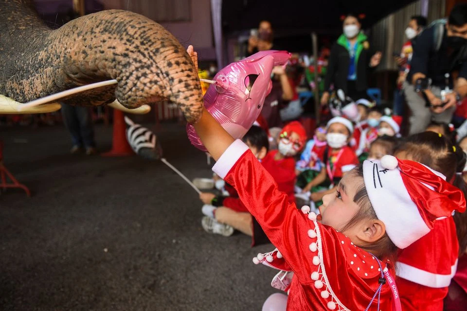 Một bé gái nhận quà Noel từ chú voi tại một trường tiểu học ở thành phố Ayutthaya (Thái Lan) ngày 23-12. Ảnh: REUTERS