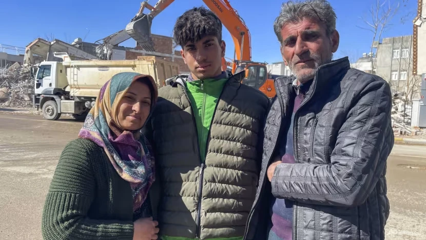 Cậu thiếu niên Taha Erdem (17 tuổi) cùng ba mẹ bên cạnh tòa nhà của gia đình bị phá hủy sau động đất ở TP Adiyaman, Thổ Nhĩ Kỳ, ngày 15-2. Ảnh: AP