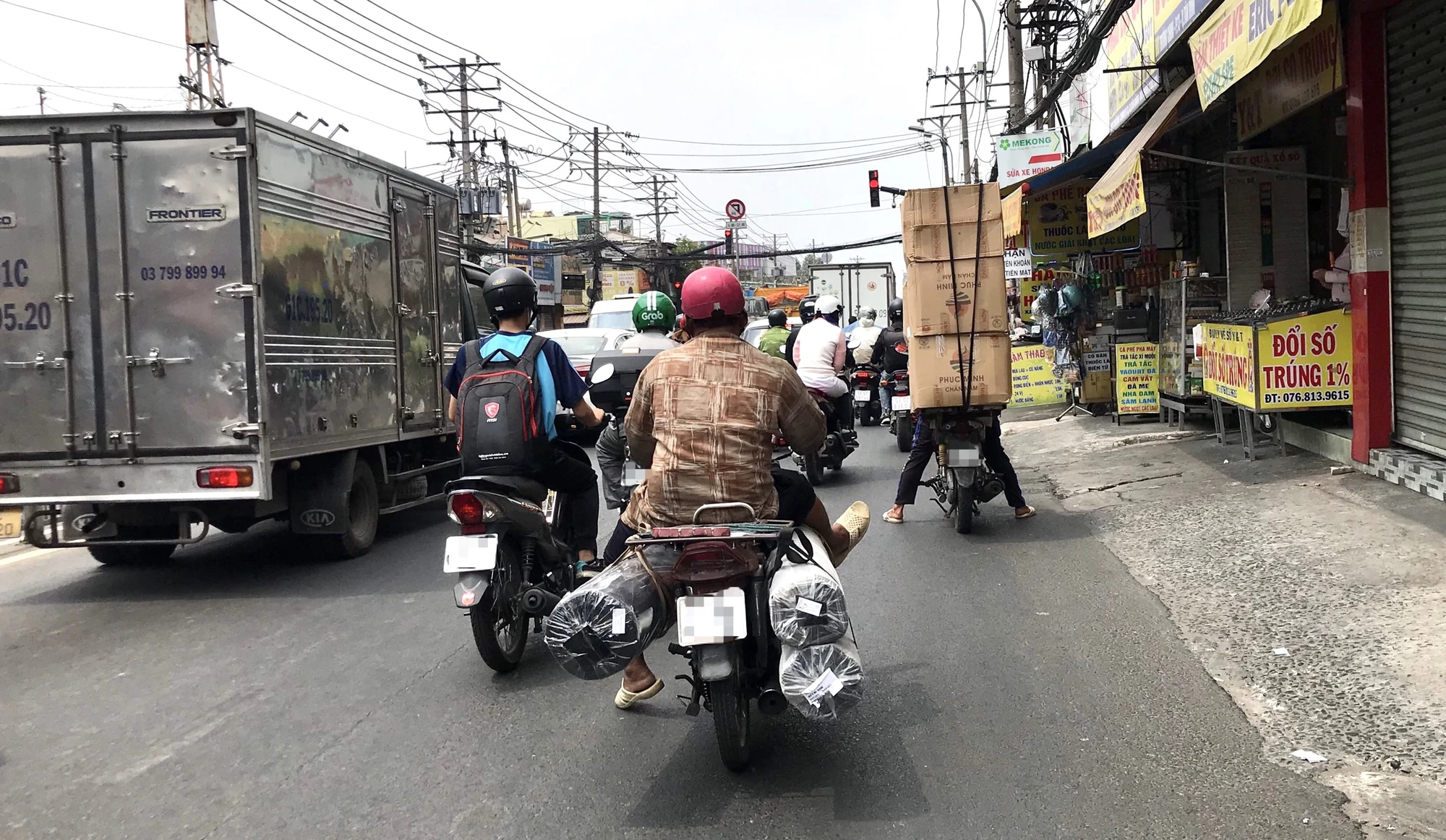 Không có chỗ gác chân, người chở hàng đành gác lên những món hàng mà mình đang chở. Phía trước là một thanh niên khác chở những thùng hàng chất cao. Ảnh: TRẦN MINH Không có chỗ gác chân, người chở hàng đành gác lên những món hàng mà mình đang chở. Phía trước là một thanh niên khác chở những thùng hàng chất cao. Ảnh: TRẦN MINH
