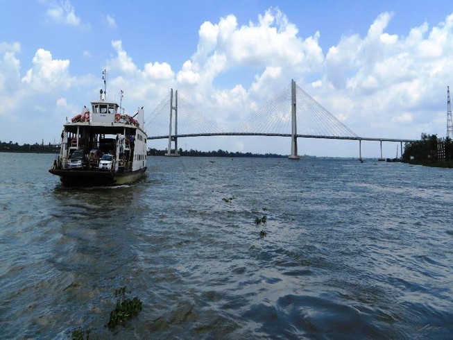 Những chuyến phà của Cụm phà Vàm Cống vẫn miệt mài qua lại đôi bờ, còn phía xa cầu Vàm Cống đã hoàn tất chờ ngày thông xe. Ảnh HOÀNG THỊ)