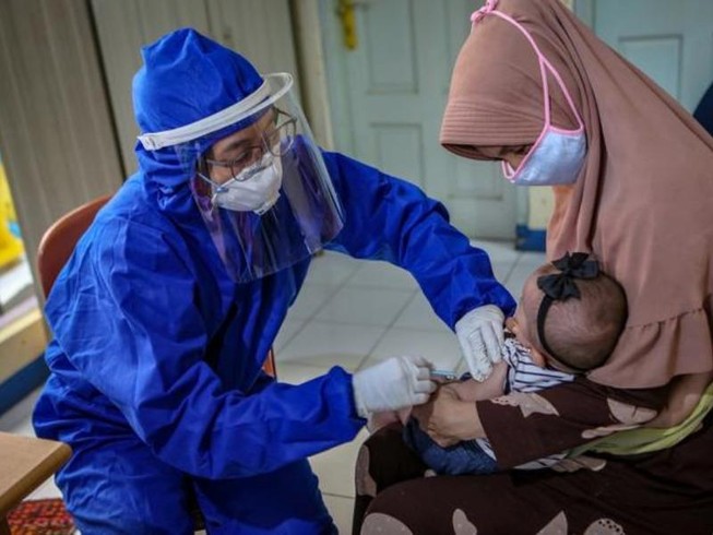 Một nhân viên y tế phải mang đồ bảo hộ để tiêm vaccine cho một em bé ở TP Tangerang, gần Jakarta, Indonesia. Ảnh: REUTERS