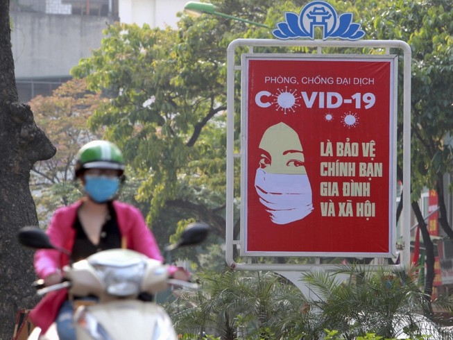 Một người dân Hà Nội chạy xe ngang qua một bảng tuyên truyền về phòng, chống dịch COVID-19 (Ảnh chụp ngày 14-4). Ảnh: REUTERS