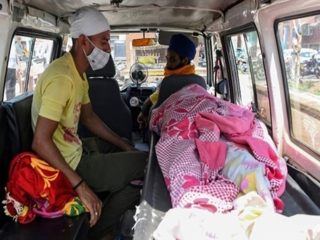 Một người ngồi bên thi thể người thân đã chết vì uống rượu lậu. Ảnh: AFP.