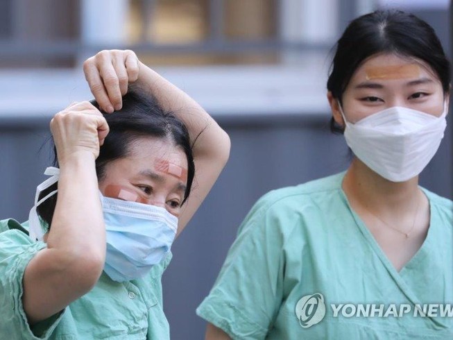 Nhân viên y tế dùng băng dính che vết thương do khẩu trang gây ra. Ảnh: YONHAP