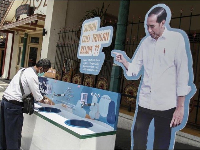 Một người rửa tay bên kệ hình Tổng thống Joko Widodo, ở TP Yogyakarta (Indonesia) ngày 30-3. Ảnh: REUTERS