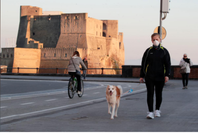 Một phụ nữ đeo khẩu trang dắt chó đi dạo ở TP Naples, vùng Campania (Ý). Ảnh: REUTERS