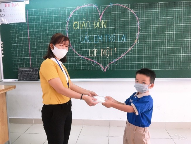 Cô giáo trao khẩu trang do TP trang bị cho học sinh trong ngày quay lại trường.