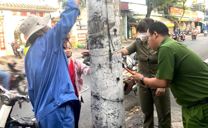 Công an phường Đông Hưng Thuận đang bóc xóa quảng cáo trái phép trên cột điện. Ảnh: TN quang-cao-trai-phep-1.jpg