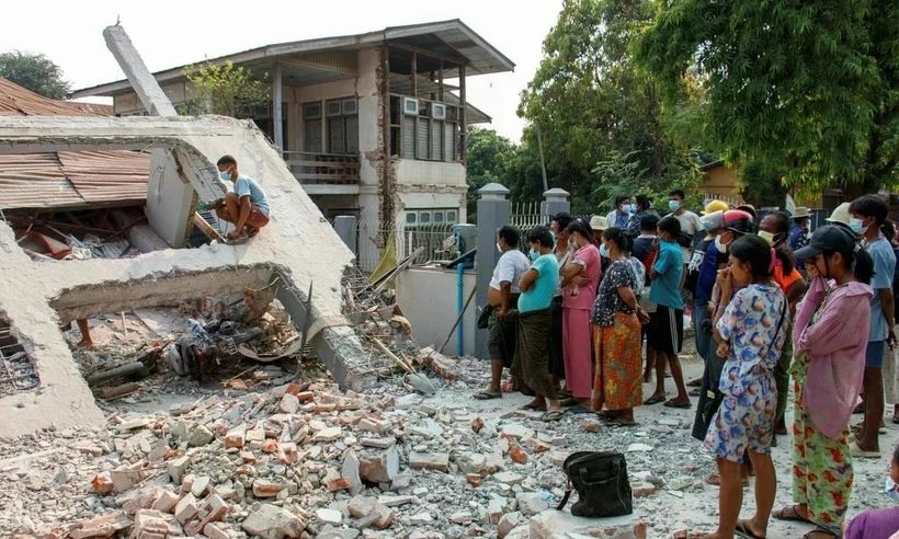 Người dân đứng bên cạnh ngôi nhà đổ nát do trận động đất Myanmar hồi tháng 3. Ảnh: THE GUARDIAN động đất Myanmar