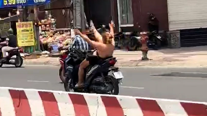 Cô gái điều khiển xe máy, không đội mũ bảo hiểm, thả hai tay, đưa chân lên trời khi đang lưu thông trên đường. Ảnh cắt từ clip Công an xác minh cô gái chạy xe máy buông hai tay, đưa chân lên trời