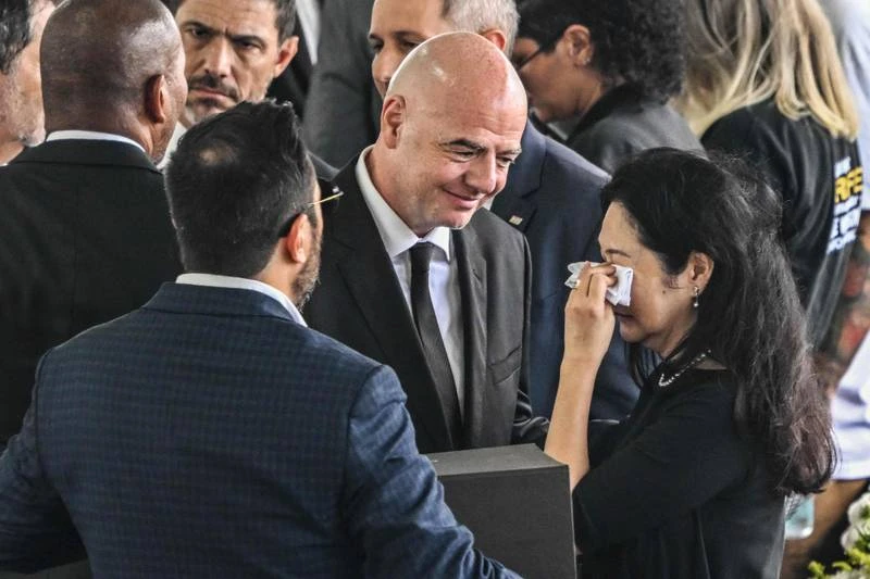 Chủ tịch FIFA Infantino chia sẻ với Marca Aoki, vợ cũ của vua bóng đá Pele. Người đứng đầu FIFA cũng chia buồn cùng con trai Edinho của Pele. Lãnh đạo CLB Santos khiêng quan tài Pele. Gam màu buồn trong tang lễ vua bóng đá. Dòng người như vô tận kéo về sân bóng CLB Santos tiễn đưa Pele. Pele là "vua của mọi tầng lớp" người dân Brazil. Bên ngoài sân bóng của Santos, nơi quàng thi thể của Pele. Quan tài Pele đi ngang qua khu vực đầy hoa. Các cựu cầu thủ, HLV của CLB Santos khiêng quan tài Pele.