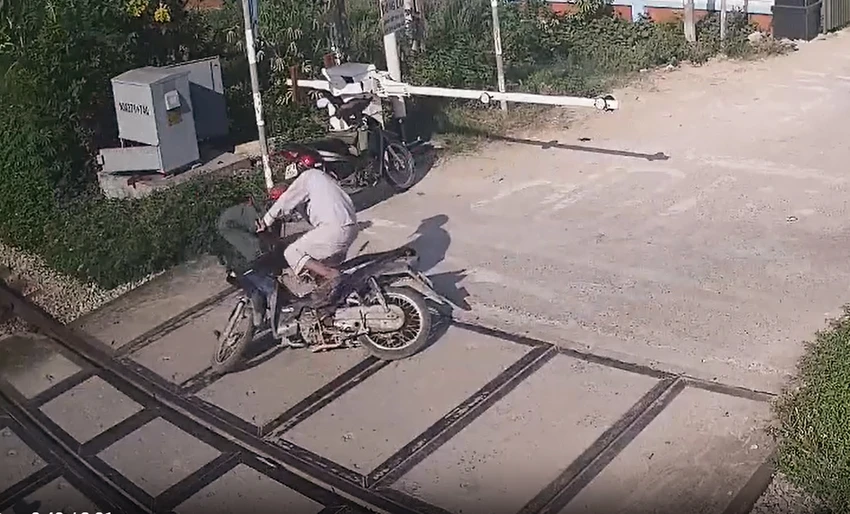 Người đàn ông đi xe máy cố vượt qua đèn đỏ, rào chắn và chuông báo hiệu khi tàu hỏa đang lao tới và nữ nhân viên đường sắt lao tới kéo ra. Ảnh: Cắt từ clip Người đàn ông đi xe máy cố vượt qua đèn đỏ, rào chắn và chuông báo hiệu khi tàu hỏa đang lao tới và nữ nhân viên đường sắt lao tới kéo ra. Ảnh: Cắt từ clip