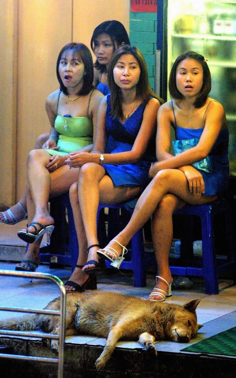 Các cô gái trẻ hành nghề mại dâm ngồi đợi khách ngoài quán bar tại phố đèn đỏ ở Bangkok.