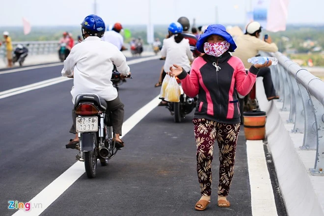 Ngay trong ngày đầu thông xe, tình trạng lộn xộn trên cầu bắt đầu xuất hiện. Chị Thanh thường bán nước mía trên bến phà Mỹ Lợi nhưng hôm nay biết cầu thông xe nên cũng lên cầu để bán cho người dân dừng xe ngắm cảnh. Con đưa di ảnh ba mẹ ngắm cầu Mỹ Lợi ngày thông xe