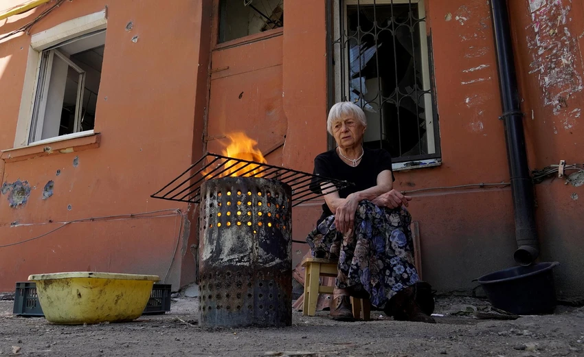 Cụ bà ngồi nấu ăn ở bên ngoài căn nhà bị hư hại vì giao tranh ở TP Mariupol. Ảnh: AFP Cụ bà ngồi nấu ăn ở bên ngoài căn nhà bị hư hại vì giao tranh ở TP Mariupol. Ảnh: AFP