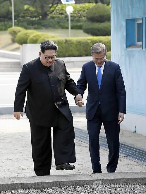 Tổng thống Hàn Quốc Moon Jae-in (phải) và lãnh đạo Triều Tiên Kim Jong-un bước lại sang phần đất Hàn Quốc sau khi bước sang phần đất Triều Tiên theo lời đề nghị của ông Kim như một biểu tượng hòa giải, tại ranh giới liên Triều ở Bàn Môn Điếm sáng 27-4. Ảnh: YONHAP