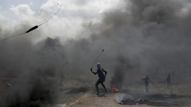 Người biểu tình Palestine ném đá vào binh sĩ Israel trong cuộc biểu tình tại biên giới Dải Gaza-Israel ngày 14-5, phản đối Mỹ chuyển đại sứ quán đến Jerusalem. Ảnh: AFP