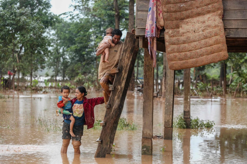 Một cặp vợ chồng mang con về lại nhà mình sau khi nước lụt rút dần ở Sanamxai, tỉnh Attapeu (Lào) ngày 26-7. Ảnh: AFP