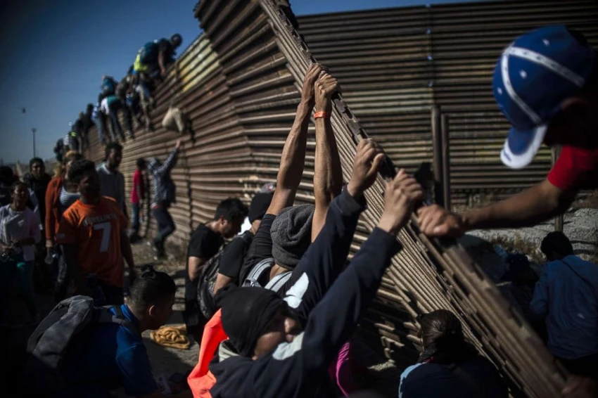 Một nhóm người di cư Trung Mỹ trèo tường ngăn biên giới Mexico-Mỹ ở TP Tijuana (Mexico) để vào Mỹ ngày 25-11. Ảnh: REUTERS
