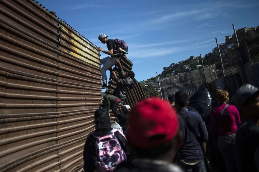 Một nhóm người di cư Trung Mỹ trèo tường ngăn biên giới Mexico-Mỹ ở TP Tijuana (Mexico) để vào Mỹ ngày 25-11. Ảnh: REUTERS