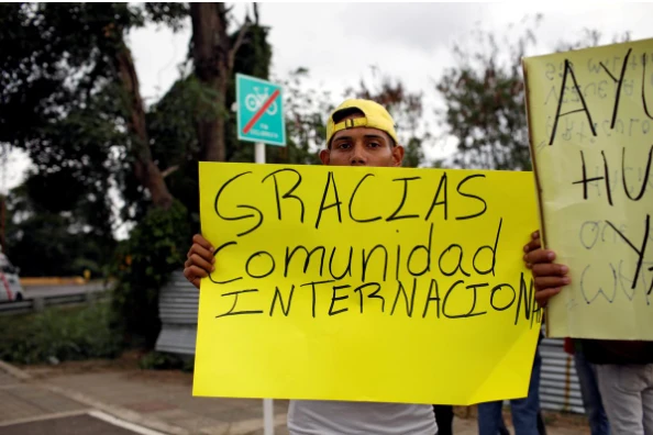 Một người dân Venezuela mang biểu ngữ có dòng chữ: “Cám ơn cộng đồng quốc tế” đứng gần một nhà kho nơi chứa hàng cứu trợ nhân đạo cho Venezuela, gần cây cầu Tienditas nối biên giới Colombia và Venezuela ở tỉnh Cucuta (Colombia) ngày 8-2. Ảnh: REUTERS
