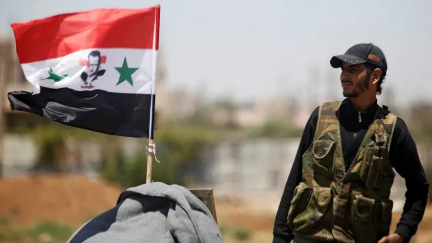 Binh sĩ quân đội Syria đứng gần cờ quốc gia Syria ở TP Deraa, tây nam Syria tháng 7-2018. Ảnh: REUTERS