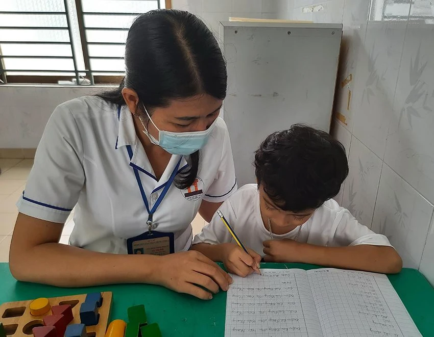 Điều dưỡng Hà Thị Mai đang tận tình hướng dẫn một trẻ tâm thần viết chữ. Ảnh: TRẦN NGỌC