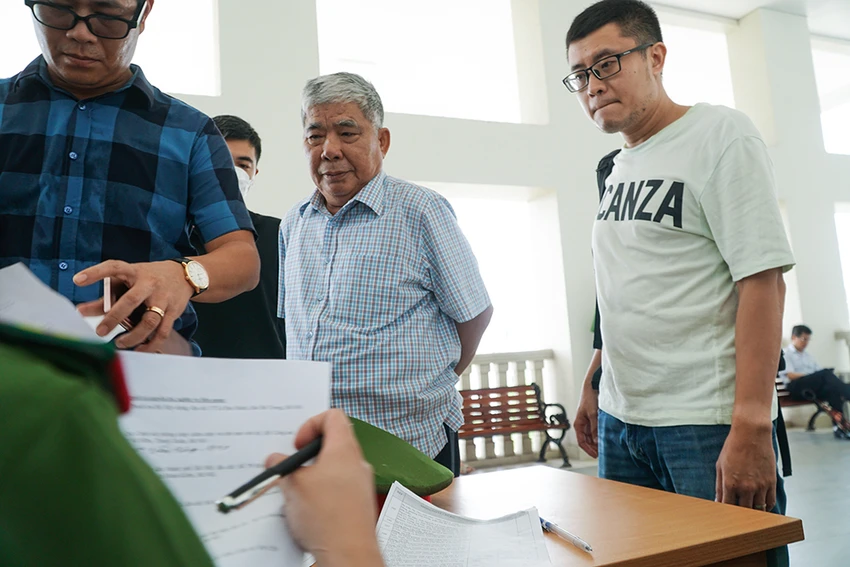 Ông Thản được kiểm tra những giấy tờ liên quan trước khi vào phòng xử án. Ông Thản được kiểm tra những giấy tờ liên quan trước khi vào phòng xử án.