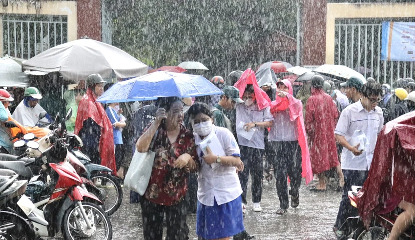 Mẹ đội ô che mưa cho con tại điểm thi Trường THCS Nguyễn Trãi, quận Gò Vấp. Ảnh minh hoạ: TRẦN MINH.